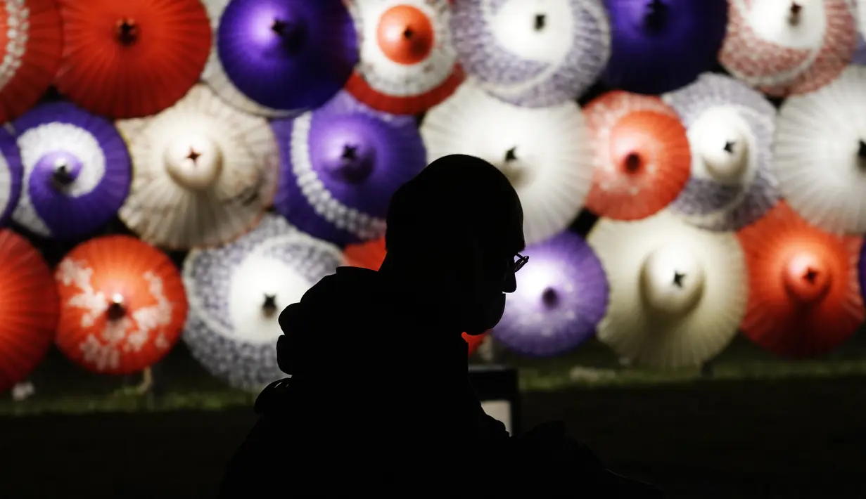 Seorang pengunjung berjalan melewati lentera berbentuk payung tradisional yang dinyalakan untuk menandai peringatan 100 tahun Kuil Meiji Jingu Shinto di Tokyo, Jumat (30/10/2020). (AP Photo/Eugene Hoshiko)