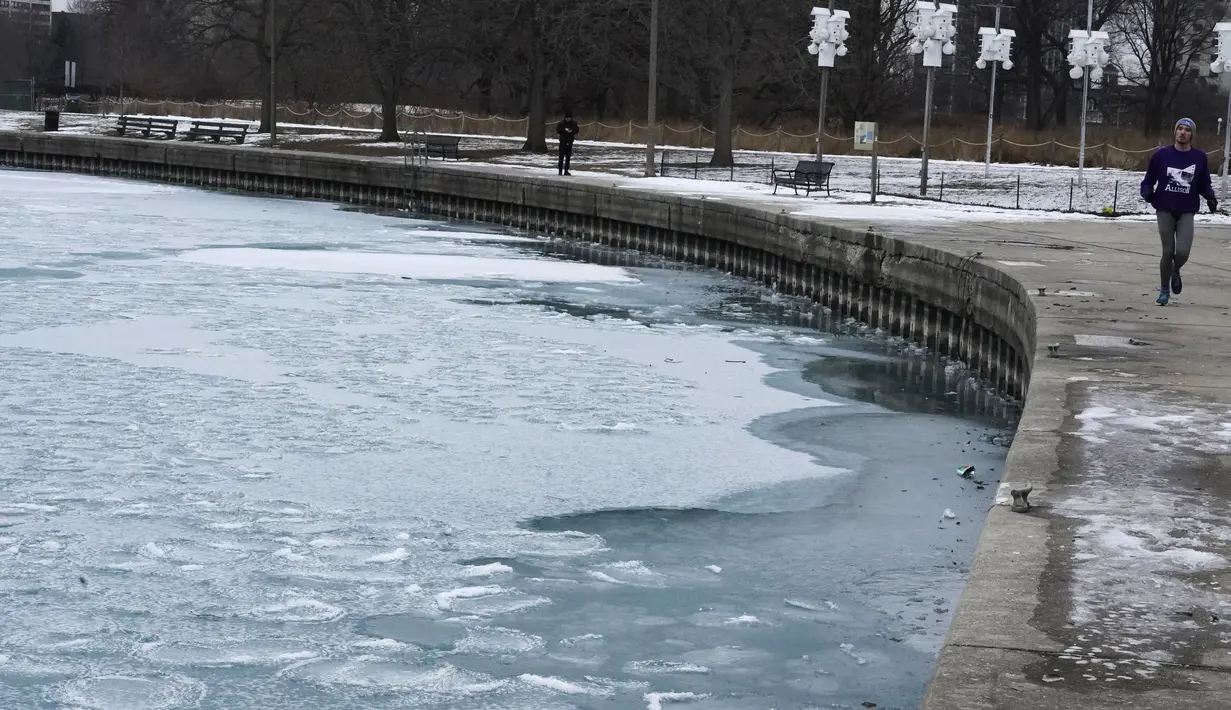 Salju dan es menutupi Danau Michigan saat seorang pria berlari di Pantai Montrose di Chicago (17/1/2022). Badai salju Chicago diperkirakan akan membawa hingga 5 inci di sepanjang Danau Michigan. (AP Photo/Nam Y. Huh)