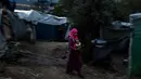 Seorang wanita imigran menggendong bayinya berjalan di luar kamp pengungsi di pulau Samsos, Yunani (13/11/2019). Ribuan imigran berjuang untuk menemukan ruang di perbukitan di atas kota, membuat rumah sementara dari bahan bangunan apa pun yang dapat mereka temukan. (AFP Photo/Angelos Tzortzinis)