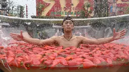 Seorang peserta berendam dalam gentong berisi cabai yang direndam air selama kompetisi makan cabai di Ningxiang, Provinsi Hunan, Tiongkok, 12 Agustus 2017. Kompetisi ini berhasil dimenangkan oleh seorang peserta yang mampu memakan 15 cabai. (STR / AFP)