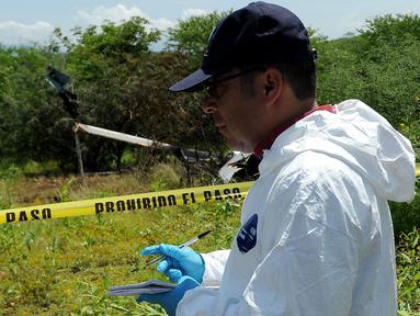 Petugas forensik berdiri di dekat puing helikopter polisi yang diduga jatuh ditembak oleh sekelompok geng kartel narkoba di Michoacan, Meksiko barat, Rabu (7/9). Insiden ini menyebabkan empat orang di helikopter tersebut tewas. (PEDRO PARDO/AFP)