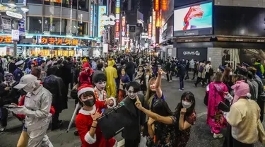 Para pejalan kaki dengan kostum berpose untuk foto ketika ribuan orang berkumpul di distrik Shibuya, area pertemuan populer untuk Halloween, di Tokyo, Minggu (31/10/2021). Daerah di sekitar Stasiun Shibuya dipadati anak-anak muda yang berdandan selama Halloween setiap tahun. (AP Photo/Kiichiro Sato)