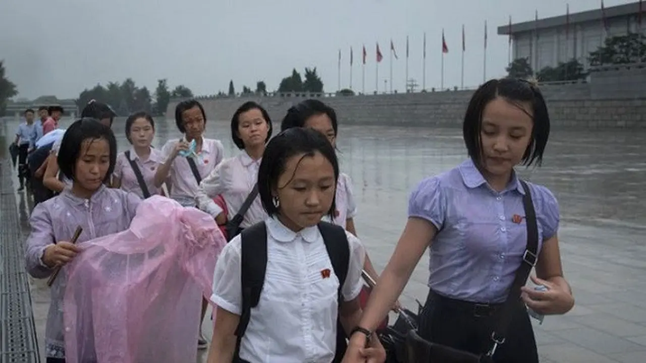 Para siswa tengah berjalan meski hujan deras untuk memberi penghormatan kepada mantan pemimpin Korea Utara Kim Il Sung dan Kim Jong-Il di luar Istana Kumsusan saat negara tersebut menandai 'Hari Kemenangan' di Pyongyang (AFP/Ed JONES)