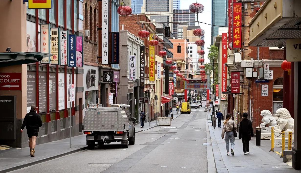 Orang-orang berjalan di jalan yang sepi di Chinatown Melbourne, ketika kota itu bersiap untuk mencabut beberapa pembatasan, Selasa (19/10/2021). Melbourne menjalani penguncian atau lockdown terpanjang di dunia, melebihi penguncian di Buenos Aires selama 234 hari. (William WEST/AFP)
