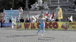 Seorang seniman sirkus tampil di depan spanduk bertuliskan "Hidup sirkus" selama demonstrasi oleh pekerja sirkus menuntut lebih banyak dukungan dari pemerintah Italia karena kegiatan mereka ditutup sejak dimulainya wabah COVID-19, di Piazza, Roma del Popolo (26/3/2021). (AP Photo/Gregorio Borgia)