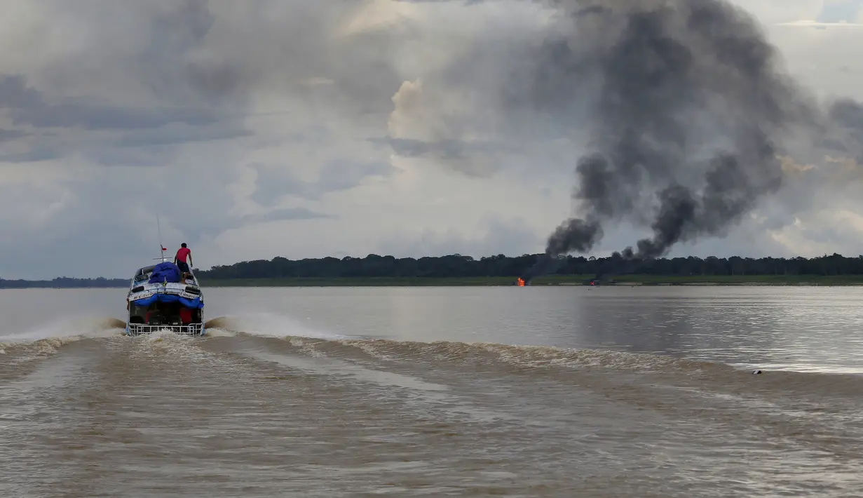 Penambang emas ilegal melintas saat asap mengepul dari tongkang di Sungai Madeira, Borba, Amazonas, Brasil, 28 November 2021. Institut Lingkungan dan Sumber Daya Alam Terbarukan Brasil membakar lebih dari 60 tongkang untuk menahan penambangan emas ilegal di anak Sungai Amazon.(AP Photo/Edmar Barros)