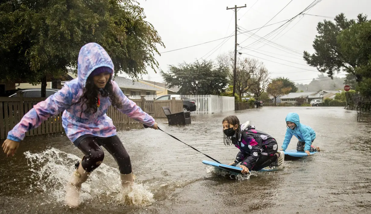 Anak-anak bermain di genangan air di Mill Valley, California, Minggu (24/10/2021). Badai kuat menerjang California Utara yang sempat mengalami kebakaran hutan, memicu tanah longsor dan banjir, juga membawa angin kencang yang merobohkan tiang-tiang listrik serta pohon tumbang. (AP Photo/Ethan Swope)