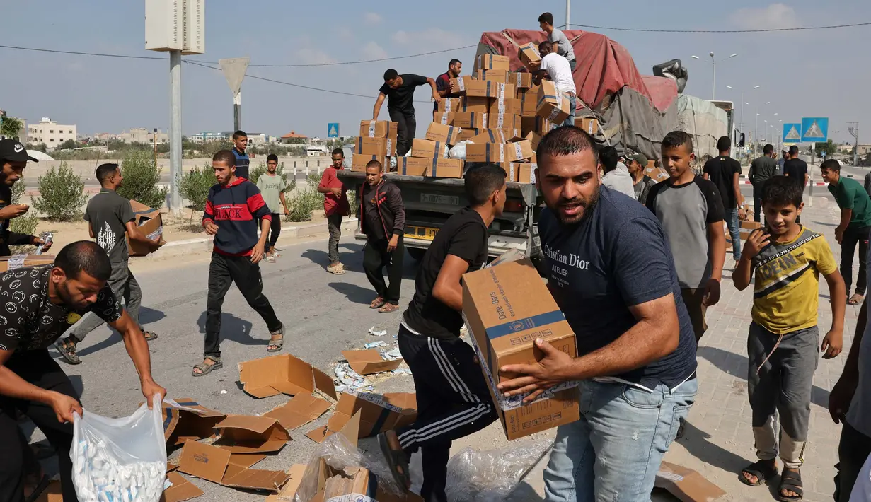 Orang-orang membongkar kotak-kotak bantuan kemanusiaan dari sebuah truk yang memasuki Jalur Gaza Selatan dari Mesir melalui penyeberangan perbatasan Rafah pada 2 November 2023. (MOHAMMED ABED/AFP)