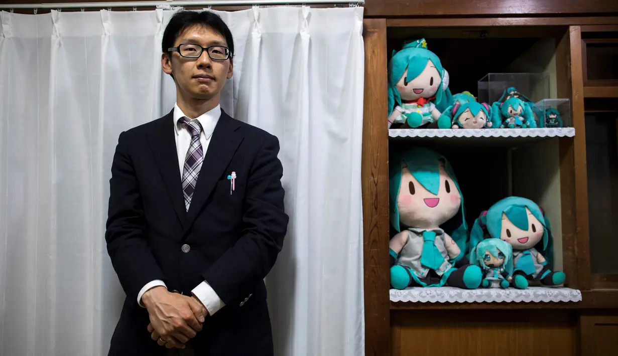 Akihiko Kondo asal Jepang berpose di sebelah boneka aktris virtual, Hatsune Miku di Tokyo, 10 November 2018. Karena masa lalunya, Kondo memutuskan untuk tak menjalin hubungan dengan manusia, dan memilih menikah dengan boneka. (Behrouz MEHRI/AFP)