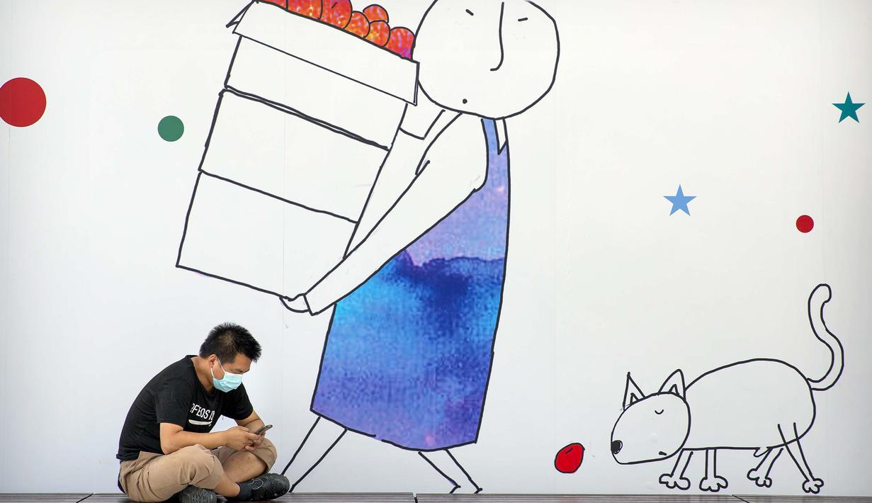 Seorang pria yang memakai masker untuk melindungi dari virus corona COVID-19 duduk di depan mural kompleks perbelanjaan dan perkantoran, Beijing, China, 11 Agustus 2020. China dan Hong Kong mengalami penurunan kasus COVID-19. (AP Photo/Mark Schiefelbein)