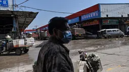 Seorang pria mengenakan masker saat berjalan di Pasar Baishazhou Wuhan di Wuhan, provinsi Hubei, Rabu (15/4/2020). Lebih dari 90 persen kios pasar basah di Wuhan telah kembali buka sejak pemerintah mencabut aturan lockdown di wilayah pusat pandemi corona tersebut. (Hector RETAMAL/AFP)