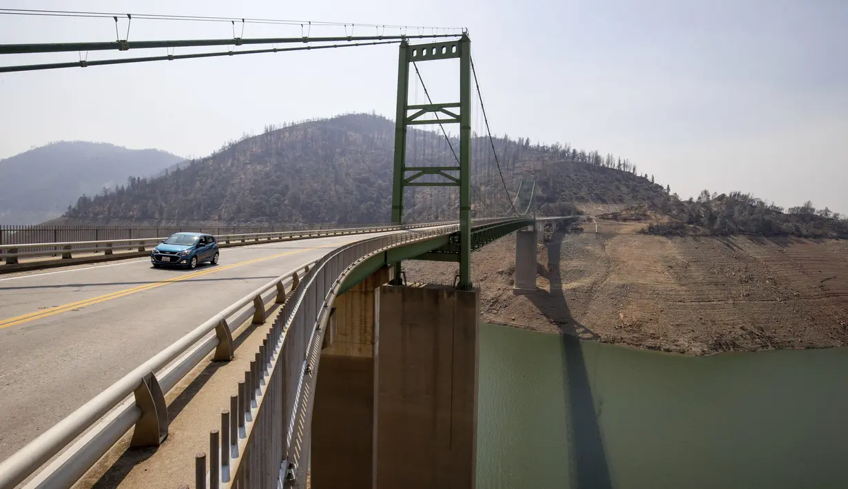 Sebuah mobil melewati Jembatan Bidwell Bar di Danau Oroville saat ketinggian air masih rendah akibat kondisi kekeringan yang terus berlanjut di Butte County, California, Minggu (228/2021). Kekeringan ekstrem di California telah membuat ketinggian air di danau itu terus menurun. (AP Photo/Ethan Swope