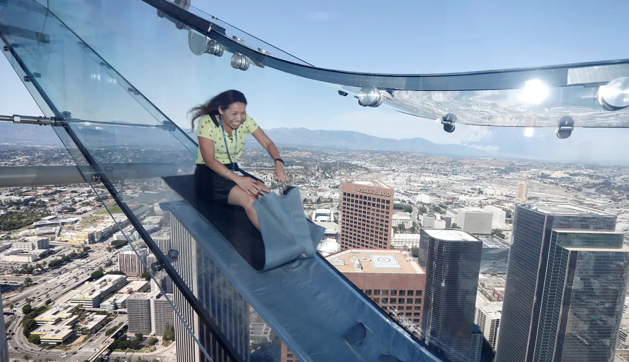Seorang wanita mencoba berseluncur menggunakan skyslide di lantai 69 dan 70 dari Bank Tower AS, Los Angeles , California, (20/6). Tempat yang dinamakan OUE Skyspace LA ini kita dapat melihat panorama indah kota LA dari atas. (REUTERS / Lucy Nicholson)