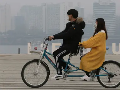 Pasangan naik sepeda menggenakan masker saat pemandangan kota diselimuti kabut tebal partikel debu halus di Seoul, Korea Selatan (5/3). Kementerian Lingkungan Korsel mengeluarkan langkah-langkah penurunan debu halus darurat. (AP Photo/Ahn Young-joon)