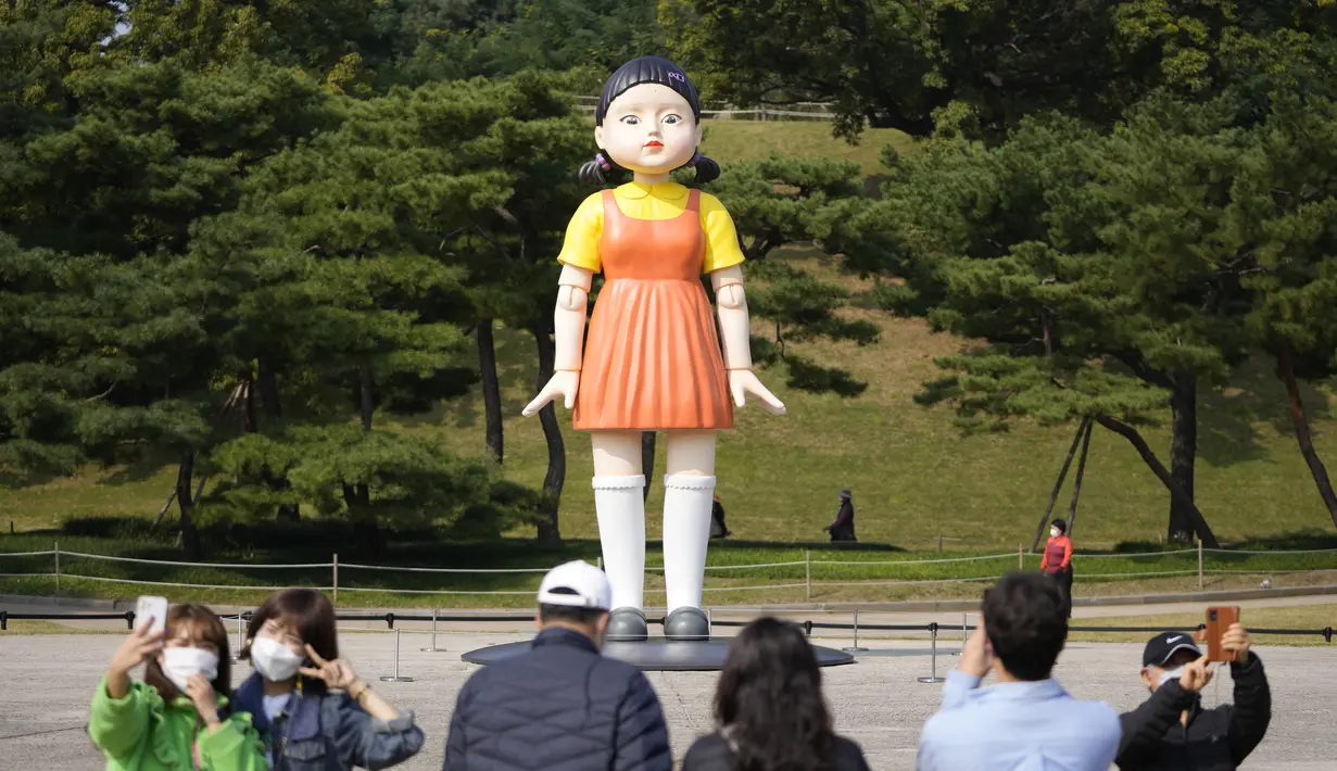 Pengunjung mengambil foto dekat boneka 'Younghee' yang menjadi maskot dalam serial Netflix asal Korea, Squid Game, di Olympic park, Seoul, Selasa (26/10/2021). Boneka setinggi empat meter atau 13 kaki itu, akan dipamerkan di taman tersebut selama tiga bulan. (AP Photo/Lee Jin-man)