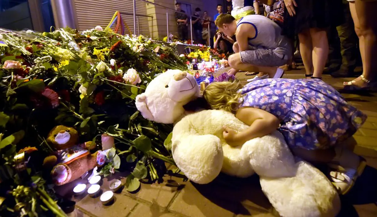 Seorang anak meletakkan boneka beruang didekat karangan bunga di depan Kedutaan Besar Belanda di Kiev, Ukraina, Jumat (17/7/14). (AFP PHOTO/Sergei Supinsky)