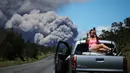 Seorang wanita berswafoto di atas mobil dengan latar belakang kepulan abu vulkanik dari gunung berapi Kilauea di Big Island Hawaii (15/5). Penduduk mendapat peringatan mengenai abu yang dapat menganggu pernapasan. (Mario Tama/Getty Images/AFP)