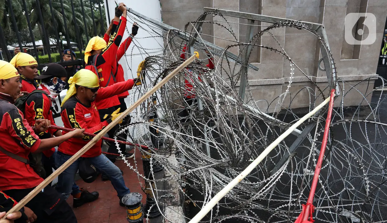 Massa merusak pagar berduri saat berunjuk rasa di depan Gedung DPR, Senayan, Jakarta, Selasa (14/3/2023). Imbas aksi demo tersebut, kepolisian mengimbau kepada para pengguna jalan untuk mencari jalan alternatif guna menghindari kemacetan. (Liputan6.com/Johan Tallo)