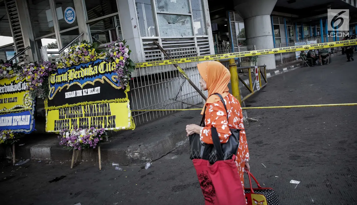 Pejalan kaki melintas dekat karangan bunga di dekat lokasi ledakan bom, Terminal Kampung Melayu, Jakarta, Kamis (25/5). Karangan bunga itu tanda duka cita pihak kepolisian terhadap tiga polisi yang gugur dan para korban luka. (Liputan6.com/Faizal Fanani)
