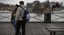 Pasangan berselfie dengan latar anggota gerakan feminis Femen yang dirantai selama aksi untuk mengecam kekerasan terhadap perempuan pada hari Valentine di pont des Arts, Paris (14/2/2020). (AFP Photo/Lionel Bonaventure)