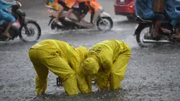 Dua petugas kota membuka selokan di jalan yang banjir setelah badai tropis Talas terjadi di Hanoi, Vietnam utara (17/7). Kondisi cuaca ini disebabkan adanya Badai Talas di perairan Laut Cina Selatan. (AFP Photo/Hoang Dinh Nam)