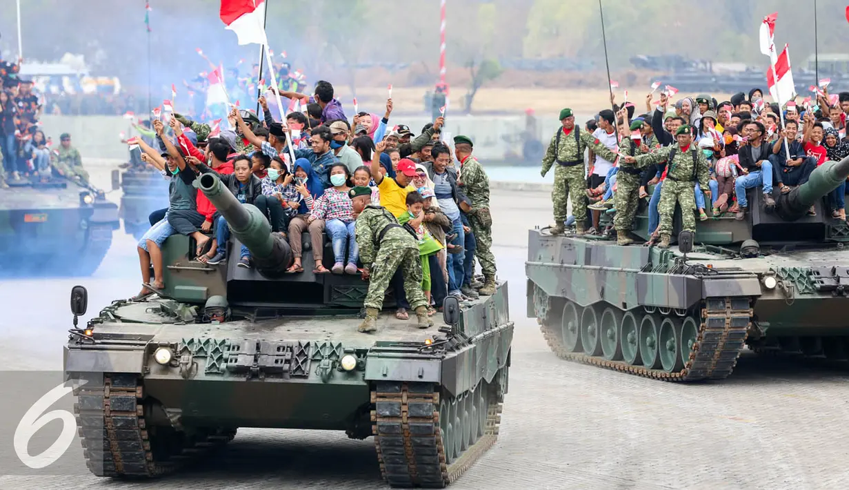 Iringan tank TNI membawa warga yang antusias menyaksikan peringatan HUT TNI ke-70 di Dermaga Indah Kiat, Cilegon, Banten, Senin (5/10/2015). HUT TNI Ke-70 ditandai atraksi tempur tiga matra TNI Angkata Darat, Laut dan Udara. (Liputan6.com/Faisal Fanani)