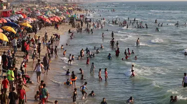 Warga Palestina berkumpul di pantai Beit Lahia di Jalur Gaza utara saat para siswa memulai liburan musim panas mereka pada 3 Juni 2022. Sejumlah warga menikmati musim panas dengan berenang dan bermain air di pantai. (MOHAMMED ABED / AFP)
