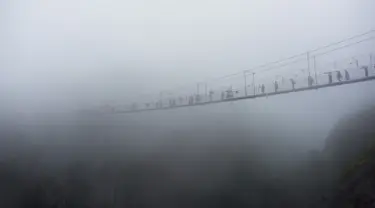 Wisatawan melewati jembatan gantung yang terbuat dari kaca di pegunungan Shinuizhai, Provinsi Hunan, Tiongkok, 6 Oktober 2015. Jembatan dengan panjang 300 m dan tinggi 180 m ini kembali dibuka setelah direnovasi untuk objek wisata. (AFP/Johannes Eisele)