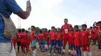 Sejumlah anak peserta coaching clinic melakukan sesi foto bersama pemain asing Malut United, Mukhammad Isaev,&nbsp;di Stadion Gelora Kie Raha, Ternate, Minggu (13/8/2023) sore hari WIT. (Bola.com/Okie Prabhowo)