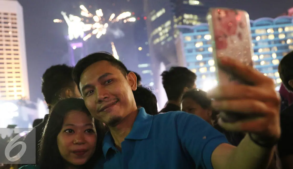 Pengunjung berselfie dengan latar belakang kembang api di kawasan Bundaran HI, Jakarta, Sabtu (31/12). Antusiasme warga menyambut tahun 2017 diramaikan dengan pesta kembang api di sejumlah sudut Ibu Kota. (Liputan6.com/Immanuel Antonius)