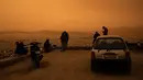 Orang-orang duduk di bukit Tourkovounia menghadap kota Athena, saat angin selatan membawa gelombang debu Sahara ke kota, di Athena, Yunani,Selasa (23/4/2024). (Angelos TZORTZINIS / AFP)