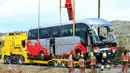Petugas menggunakan crane untuk memindahkan bangkai bus ke truk tailer di Jalan Raya AP7 dekat Kota Freginals, Spanyol, Minggu (20/3). Bus berisi 57 mahasiswa asing itu terbalik ketika dalam perjalanan dari Valencia menuju Barcelona (PAU Barrena/AFP)