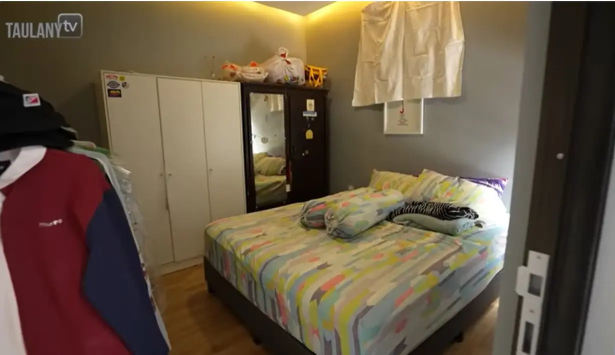Naik ke lantai dua ada dua kamar, gudang dan tempat untuk mencuci dan jemuran. Potret berikut merupakan kamar yang digunakan Gilang. Menurutnya, kamar ini sebenarnya milik adiknya. Di kamar ini juga penuh dengan pakaian yang digantung. [Youtube/TAULANY TV]