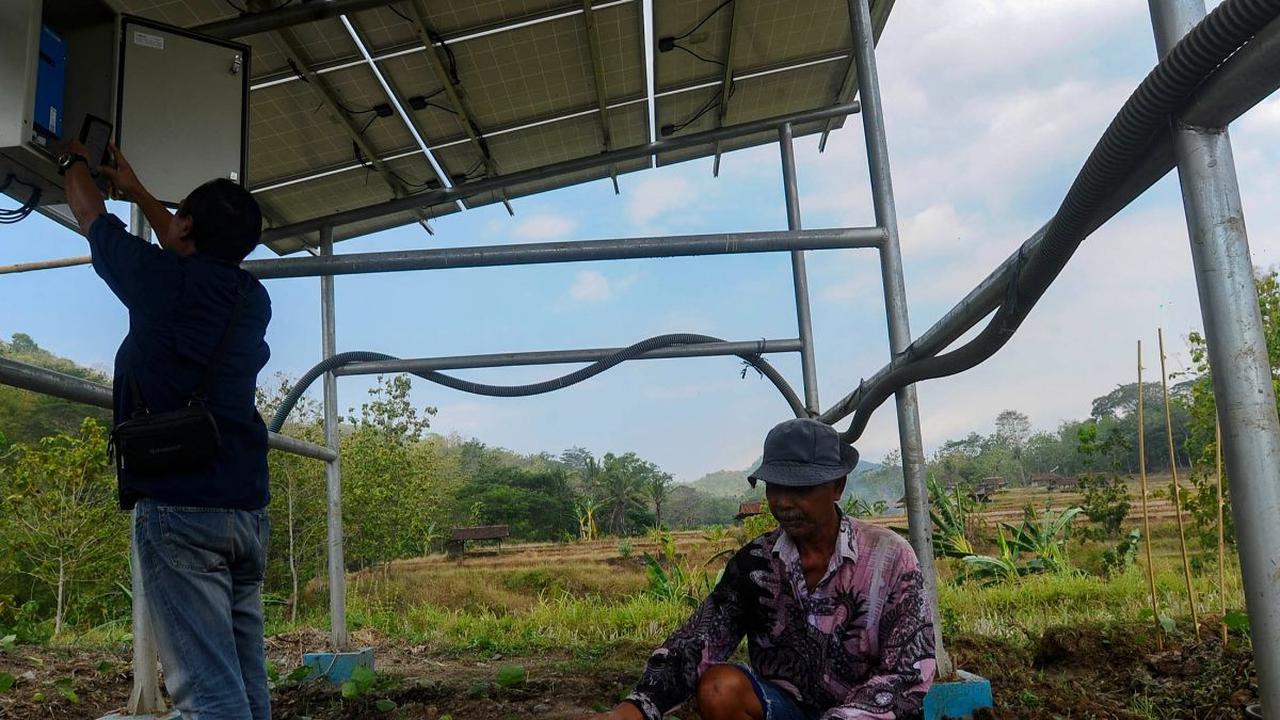 Seorang petani beraktivitas melakukan penyiraman saat Petugas dari Green Energy Nusantara Mandiri sedang melakukan pengecekan pada salah satu alat elektronik pada panel surya.