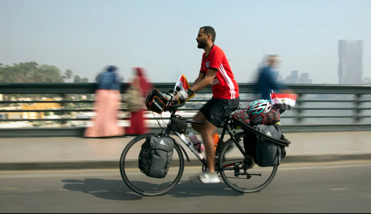 Seorang pria Mesir, Mohammed Nufal (24) mengendarai sepedanya melintasi jembatan Qasr El-Nile di Kairo, Sabtu (7/4). Nufal mengayuh sepedanya sejauh 5000 kilometer menuju Rusia, demi mendukung timnas Mesir di Piala Dunia 2018. (AP/Amr Nabil)