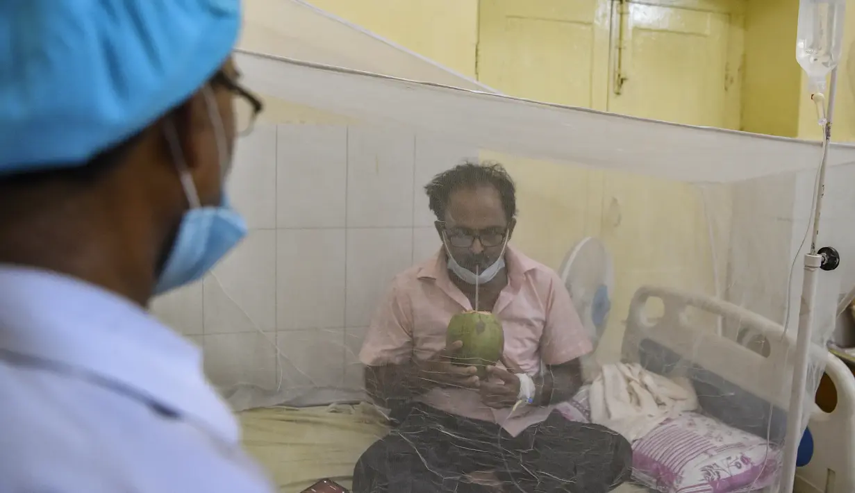 Petugas medis melihat seorang pasien minum air kelapa saat dia duduk di bawah kelambu di bangsal demam berdarah sebuah rumah sakit pemerintah di Allahabad, India (30/8/2021). (AFP/Sanjay Kanojia)