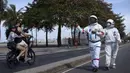 Akuntan Brasil Tercio Galdino (66) memberi isyarat jempol kepada warga yang mengendarai sepeda motor saat dia dan istrinya Alicea Galdino berjalan di sepanjang pantai Leme dengan pakaian pelindung mirip astronaut, Rio de Janeiro, Brasil, 12 Juli 2020. (Mauro Pimentel/AFP)