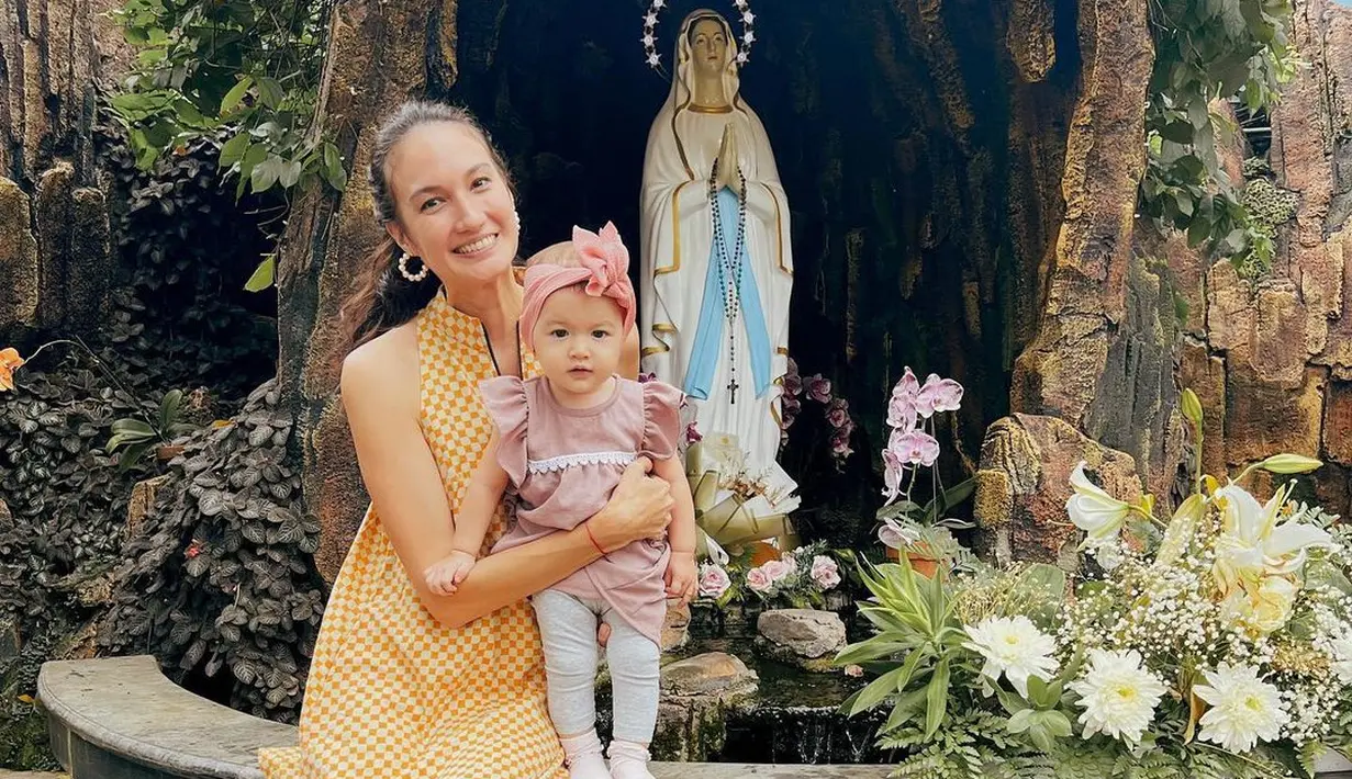 Berpose manis di depan patung Bunda Maria, kedua tampil serasi dengan outfit masing-masing. Nadine memilih dress pendek tanpa lengan bermotif kotak-kotak kuning, sedangkan sang buah hati tampak mengenakan dress mini yang gemas berwarna ungu, dengan legging abu-abu, dan hiasan kepala yang menambah kesan gemas. Foto: Instagram.