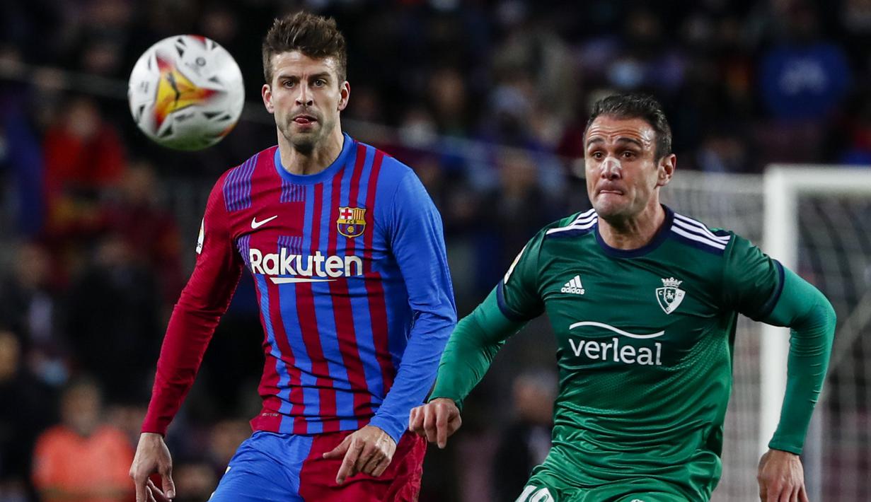Bek Barcelona, Gerard Pique berebut bola dengan pemain Osasuna, Kike Garcia selama pertandingan lanjutan La Liga Spanyol di di stadion Camp Nou di Barcelona, Senin (14/3/2022). Barcelona menang telak atas Osasuna 4-0. (AFP/Josep Lago)