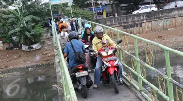 Warga serta pengendara motor menyeberangi Kanal Banjir Barat (KBB) di kawasan Tanah Abang, Jakarta, Jumat (30/12). Tidak tersedianya fasilitas penyeberangan lain membuat warga serta pengendara harus berbagi jalan. (Liputan6.com/Immanuel Antonius)