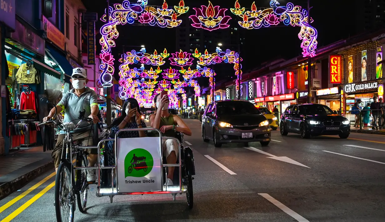 Para penumpang dengan menggunakan becak berkeliling di distrik Little India yang dihias dekorasi meriah menjelang Diwali, festival cahaya bagi umat Hindu, di Singapura pada 23 Oktober 2020. (Photo by Roslan RAHMAN / AFP)