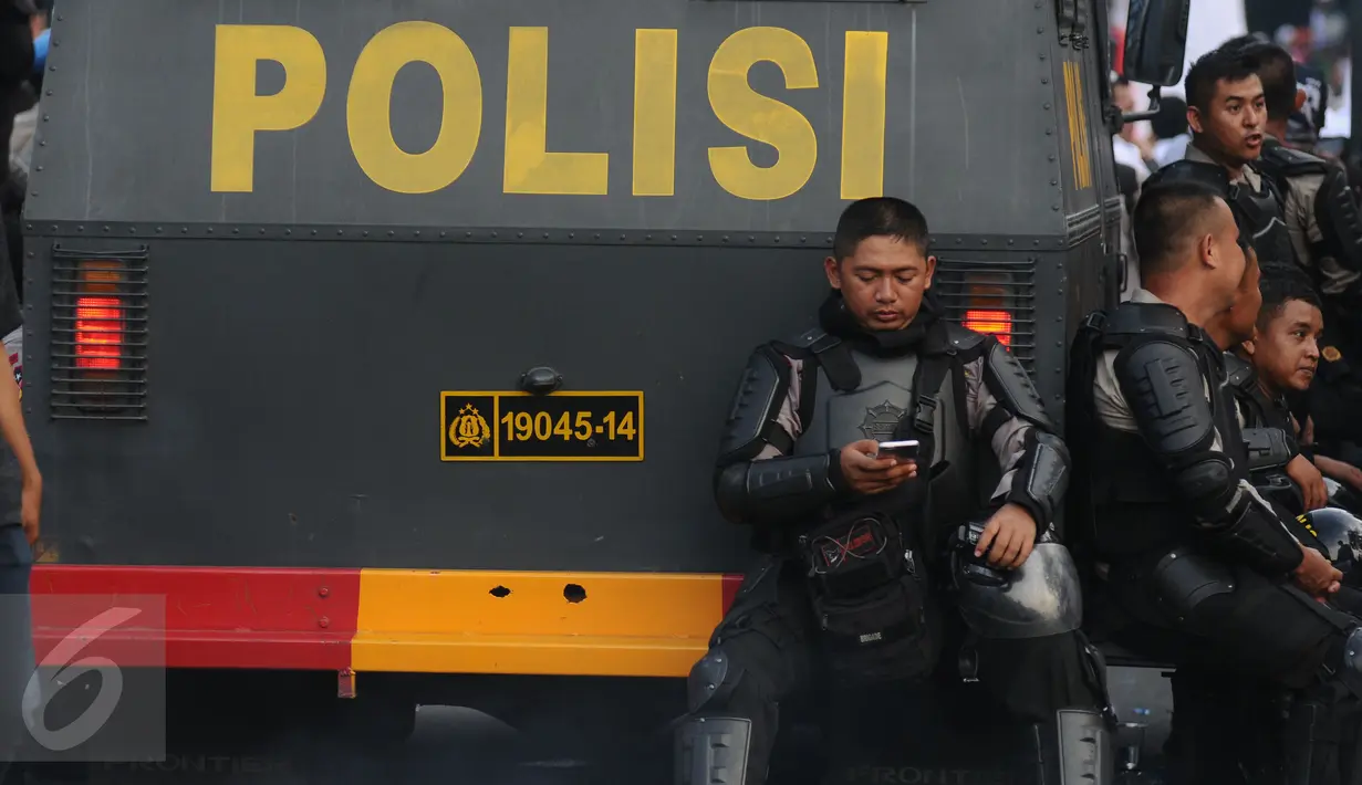 Polisi beristirahat sambil melihat ponsel di depan Istana Negara, Jakarta, Jumat (4/11). Ribuan aparat gabungan disiagakan saat massa melakukan aksi menuntut penegakan hukum kasus dugaan penistaan agama. (Liputan6.com/Helmi Fithriansyah)