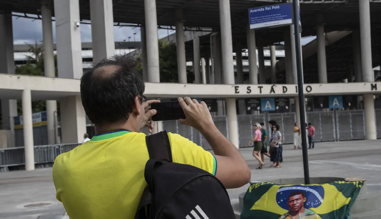 Seorang pria mengambil foto plang dengan nama baru jalan yang mengelilingi stadion Maracana, yang sekarang akan dikenal sebagai King Pele Avenue di Rio de Janeiro, Brasil, 4 Desember 2022. Perubahan nama tersebut sebagai penghargaan untuk legenda sepak bola Brasil, Edson Arantes do Nascimento atau lebih dikenal sebagai Pele. (AP Photo/Bruna Prado)