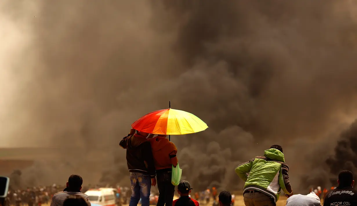 Warga melihat kepulan asap hitam yang membubung saat mereka menggelar aksi protes di perbatasan Palestina-Israel di kota Gaza tengah (13/4). (AFP/Mohammed Abed)