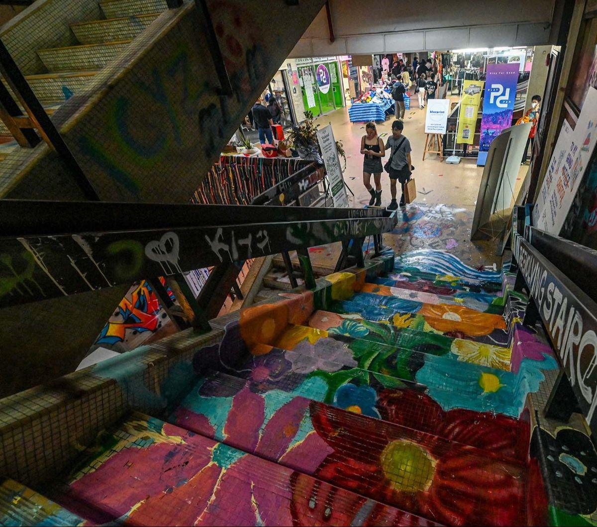Pengunjung berjalan di dekat anak tangga penuh warna di Peace Centre, sebuah mal terbengkalai yang berubah menjadi kawasan seni tak terduga, di Singapura, pada 19 Januari 2024. Grafiti merupakan hal yang terlarang di Singapura. Para pelakunya terancam men