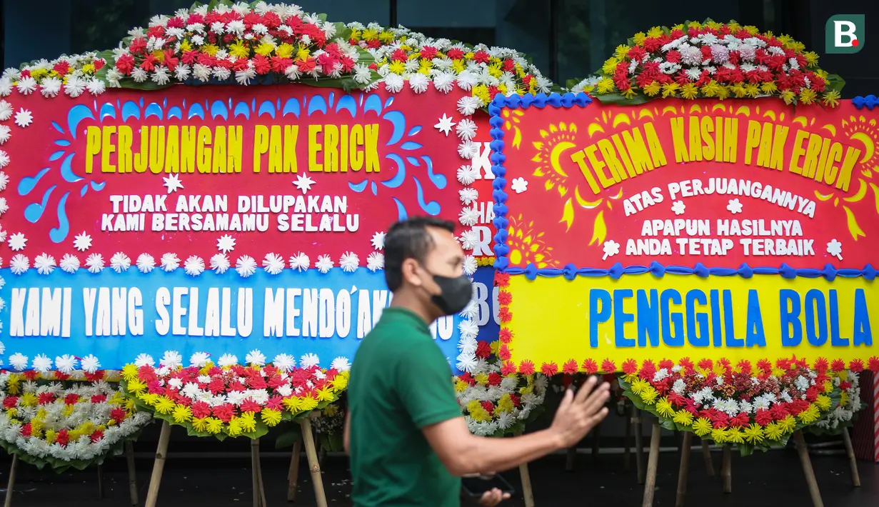 Seorang petugas melewati karangan bunga yang membanjiri kantor PSSI di GBK Arena, Senayan, Jakarta, Kamis (30/03/2023) sebagai respon pembatalan Indonesia sebagai tuan rumah Piala Dunia U-20 2023 oleh FIFA. (Bola.com/Bagaskara Lazuardi)