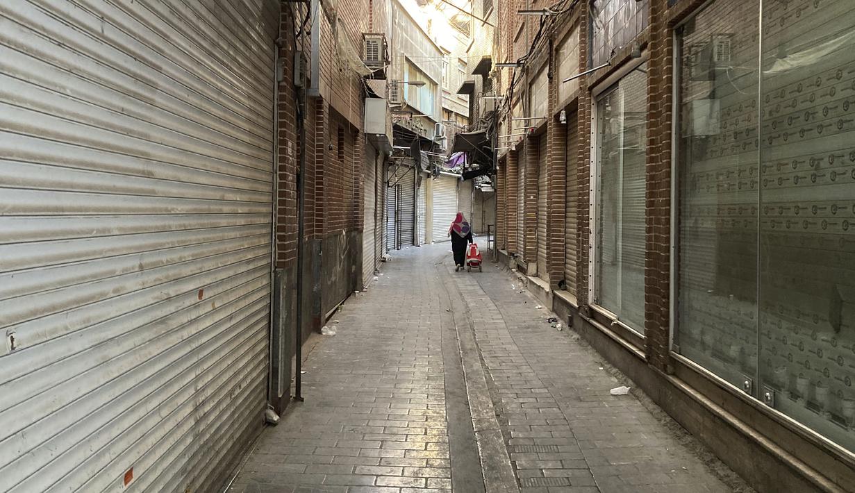Seorang perempuan membawa gerobaknya melewati toko-toko yang tutup di Grand Bazaar Teheran, Iran, Selasa (15/11/2022). Banyak toko di Grand Bazaar di ibu kota Iran ditutup Selasa di tengah seruan mogok menyusul kematian seorang perempuan pada September lalu yang ditangkap oleh polisi moral Iran. (AP Photo/Vahid Salemi)