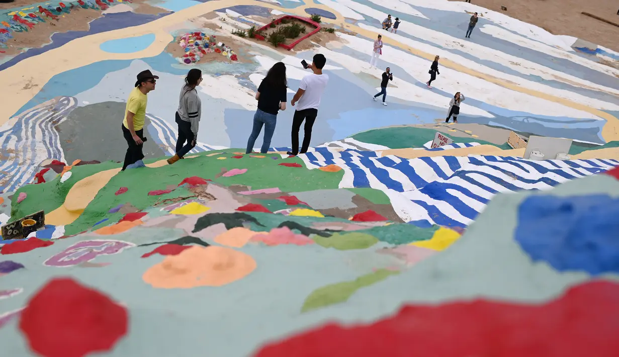 Turis mengunjungi Salvation Mountain, sebuah lereng bukti di Niland, California, Amerika Serikat. Salvation Mountain memiliki lebar 46 meter, dan panjang 15,2 meter ini tidak dihiasi pepohonan, melainkan tulisan dan gambar warna-warni dengan pesan cinta. (Robyn Beck/AFP)