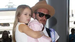 Harper Beckham digendong ayahnya saat berada di bandara LAX menuju London pada 31 Agustus 2015. Harper tampil manis dengan menggunakan dress putih polos. (harperbeckhamfashion)