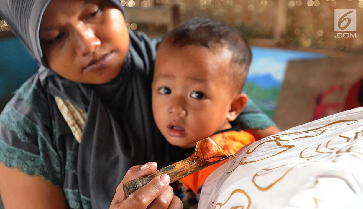 Seorang ibu menggendong anaknya sambil membuat batik tulis di Kampung Batik Puswasedar kawasan Geopark Ciletuh, Sukabumi, Jawa Barat, Sabtu (22/9). Motif batik digali dari beragam sumber Geopark Ciletuh. (Merdeka.com/Arie Basuki)